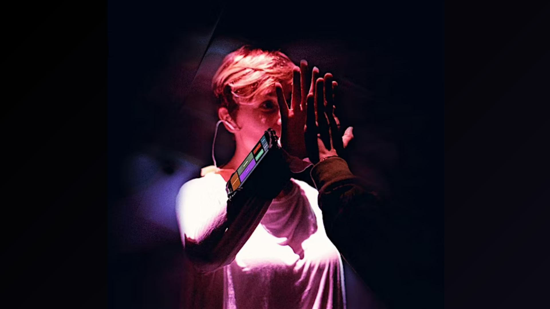 Person touching hands with another against a dark background, wearing a haptic device on their wrist.