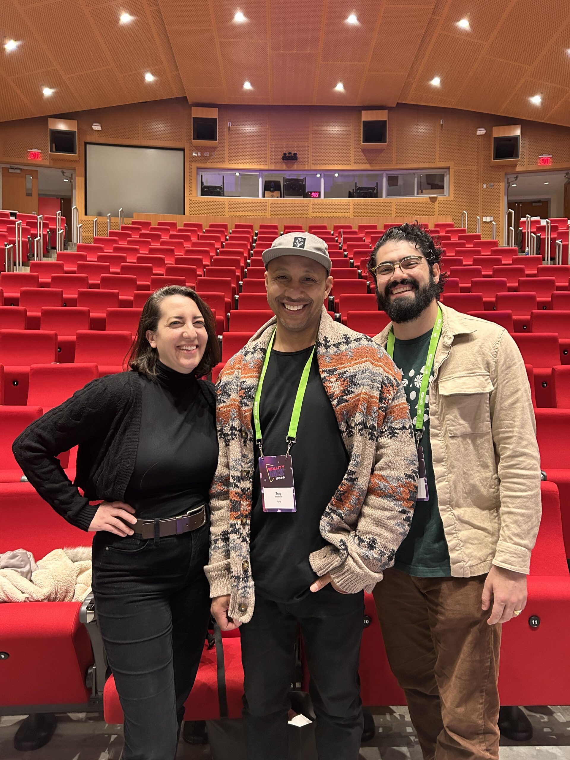 Vanessa, Tory Stephens, and Raul smile with Hackathon badges around their necks. 