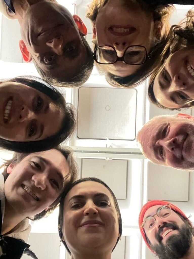 Eight people take a selfie looking down into a camera. 