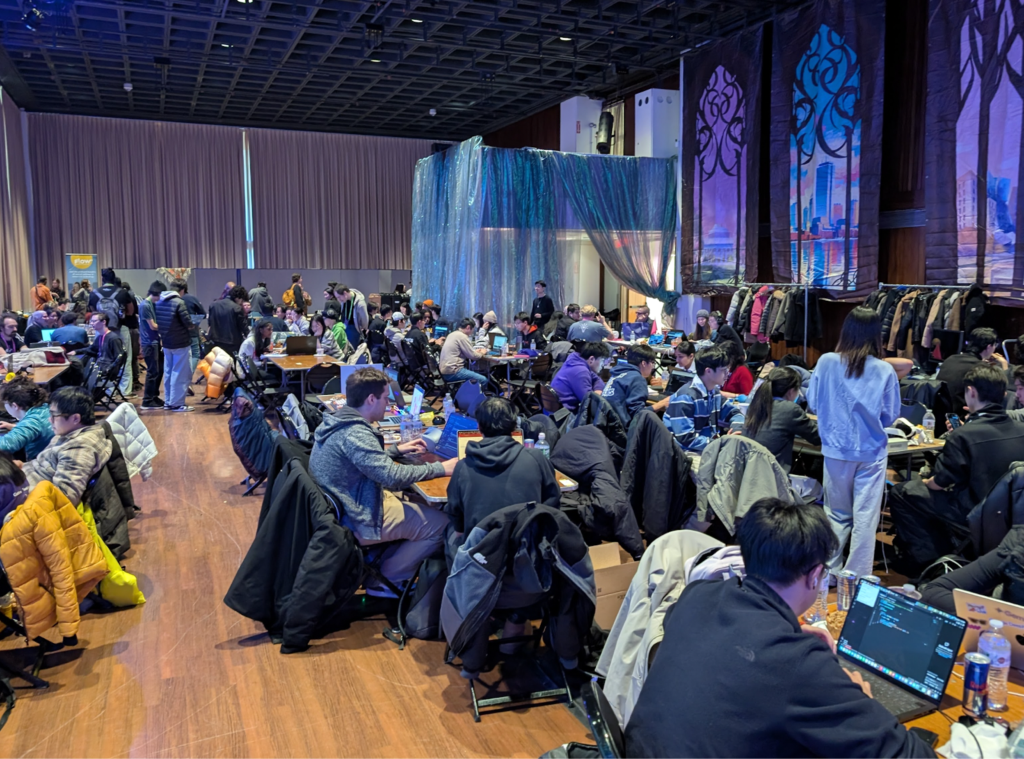 A crowd of participants hack away in a crowded hall. 