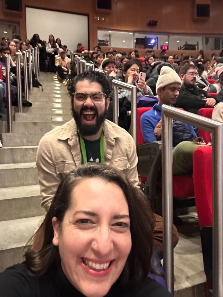 Raul and Vanessa sit on the stairs in the middle of an auditorium packed with people. 
