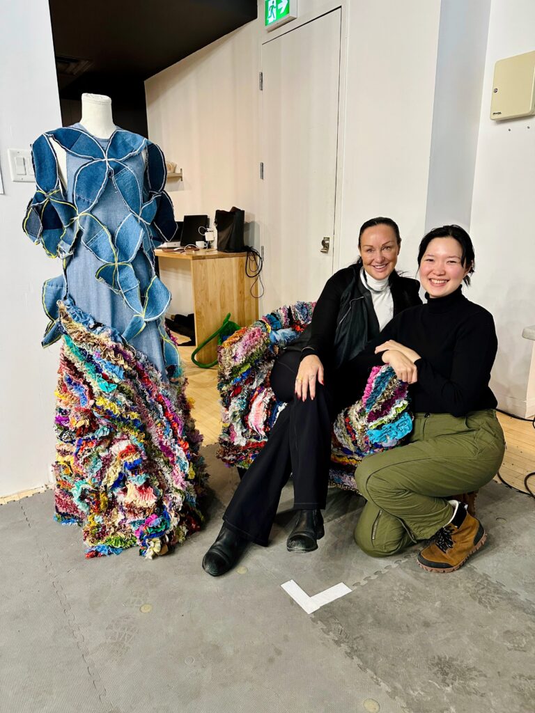 Phoebe sits in the ruffled fabric chair and Mira kneels next to her. 