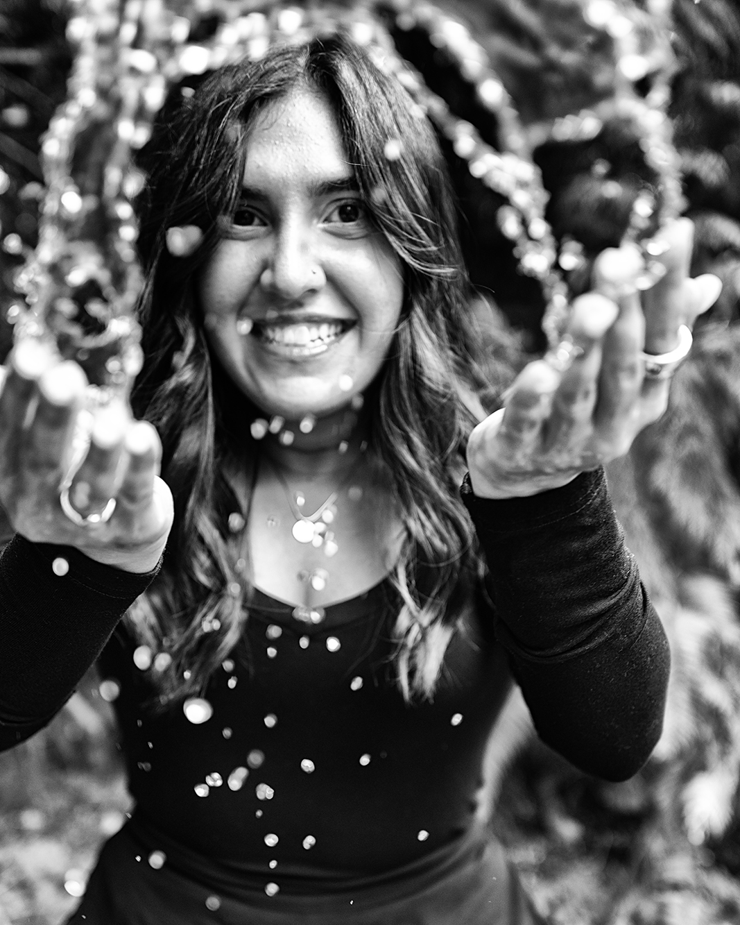 Woman tossing water in cupped hands, standing outdoors in a wooded area, black-and-white photo