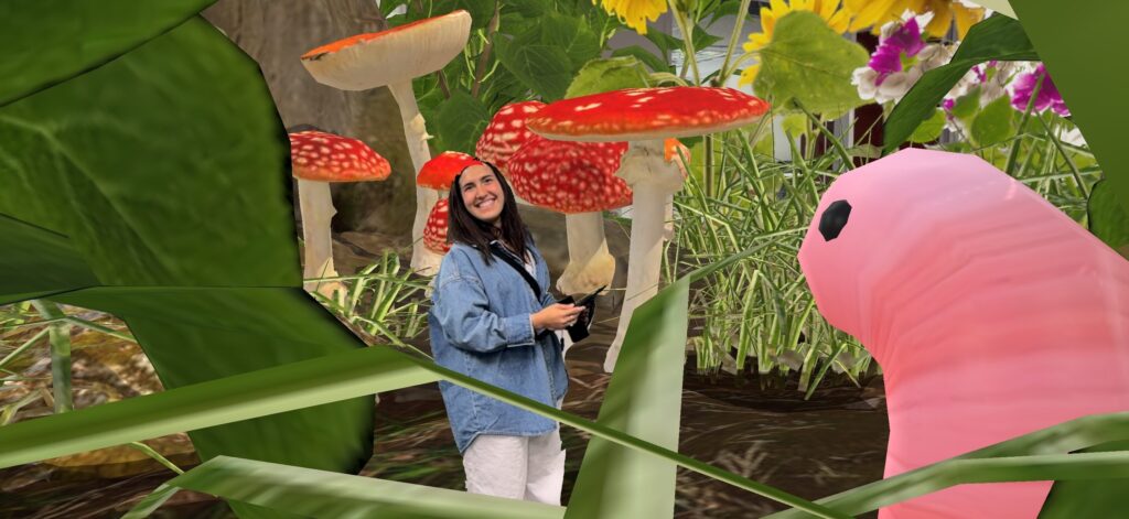 alt="Smiling woman in a denim jacket stands near giant red-capped mushrooms and flowers, with a pink worm creature beside her, agog logo below"