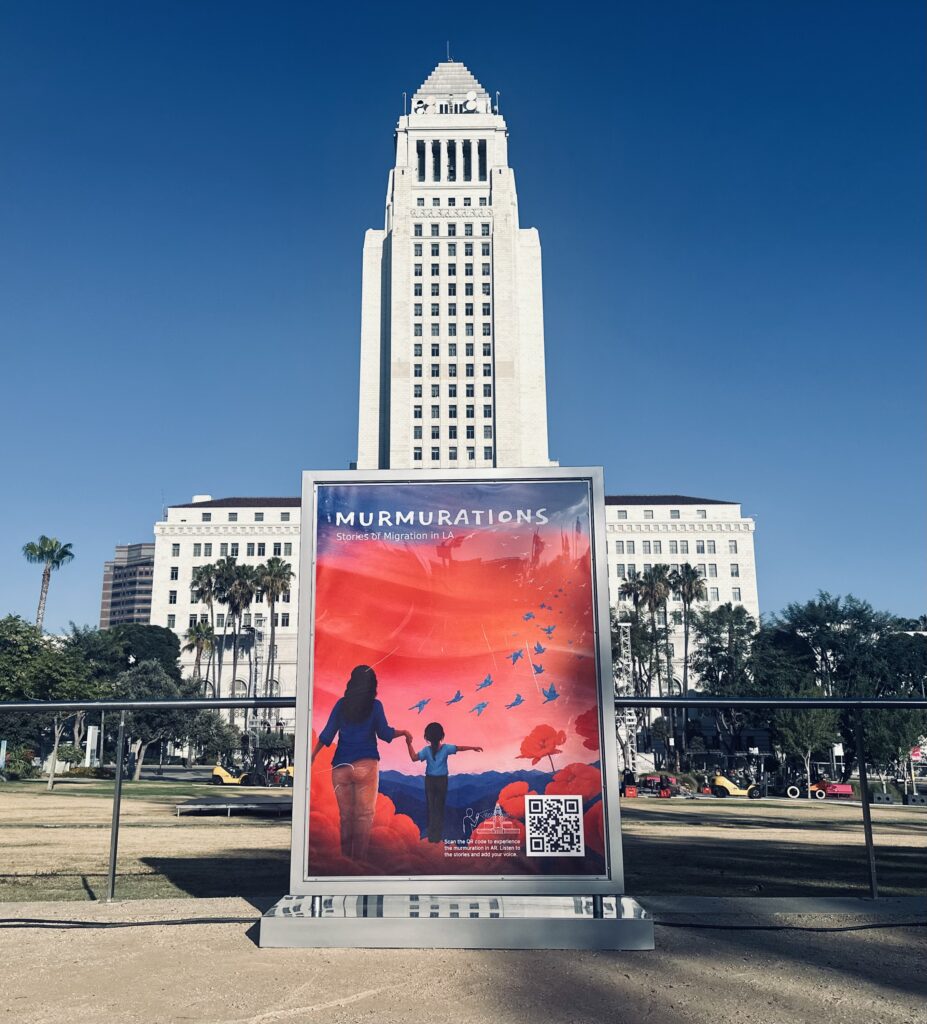 alt="'Murmurations: Stories of Migration in LA' poster with a QR code, showing an illustrated adult and child releasing birds, displayed outside LA City Hall"