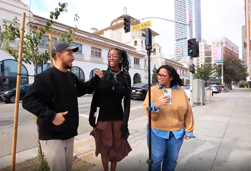 Three people laughing together on a city sidewalk, filming with a 360 camera.